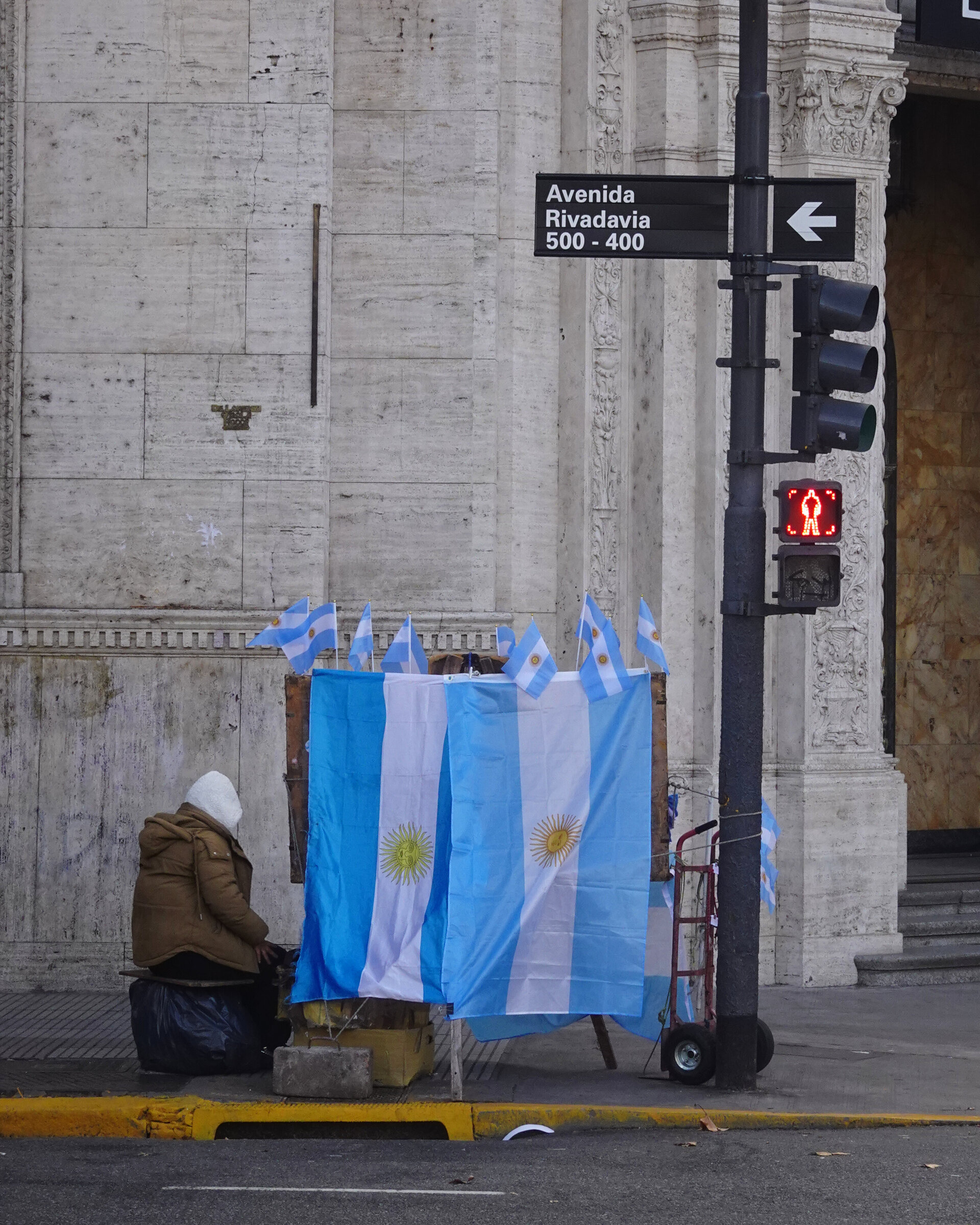 A vendor sitting beside a stall of Argentine flags on Avenida Rivadavia