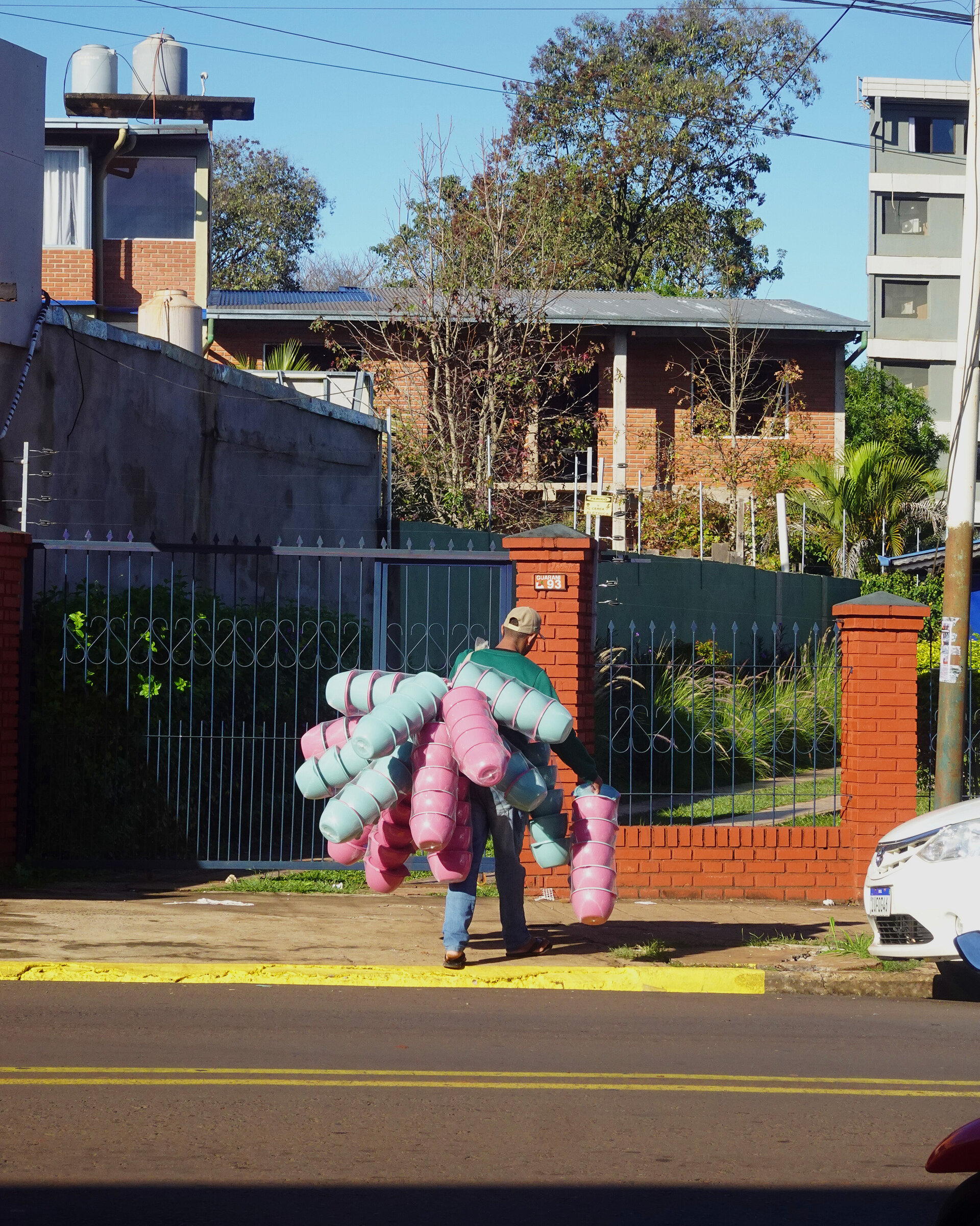 A street vendor carrying stacks of pink and green plastic buckets