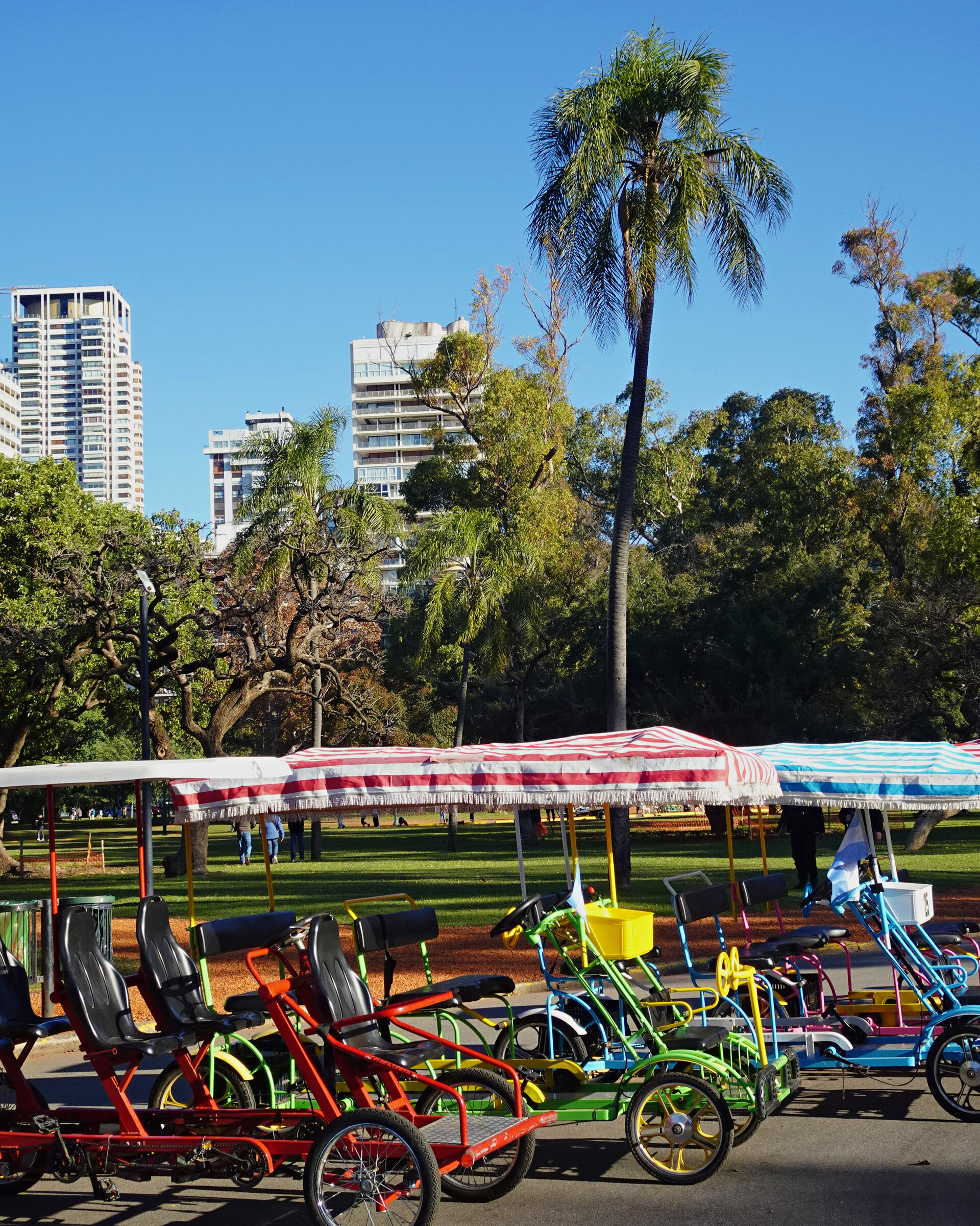 A row of brightly coloured pedal cars under striped canopies in a city park