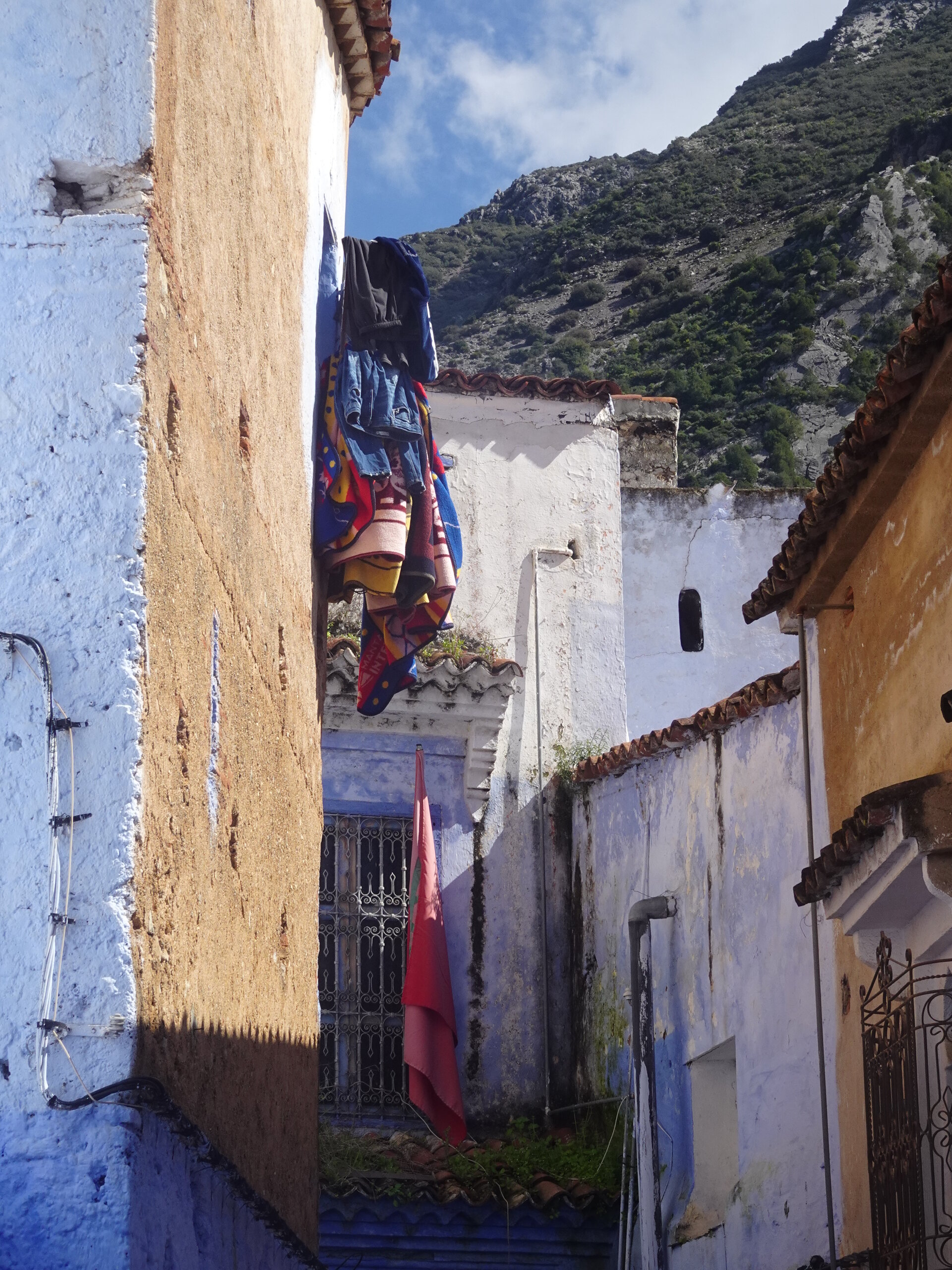 Narrow alley with laundry hanging between blue walls and mountain above