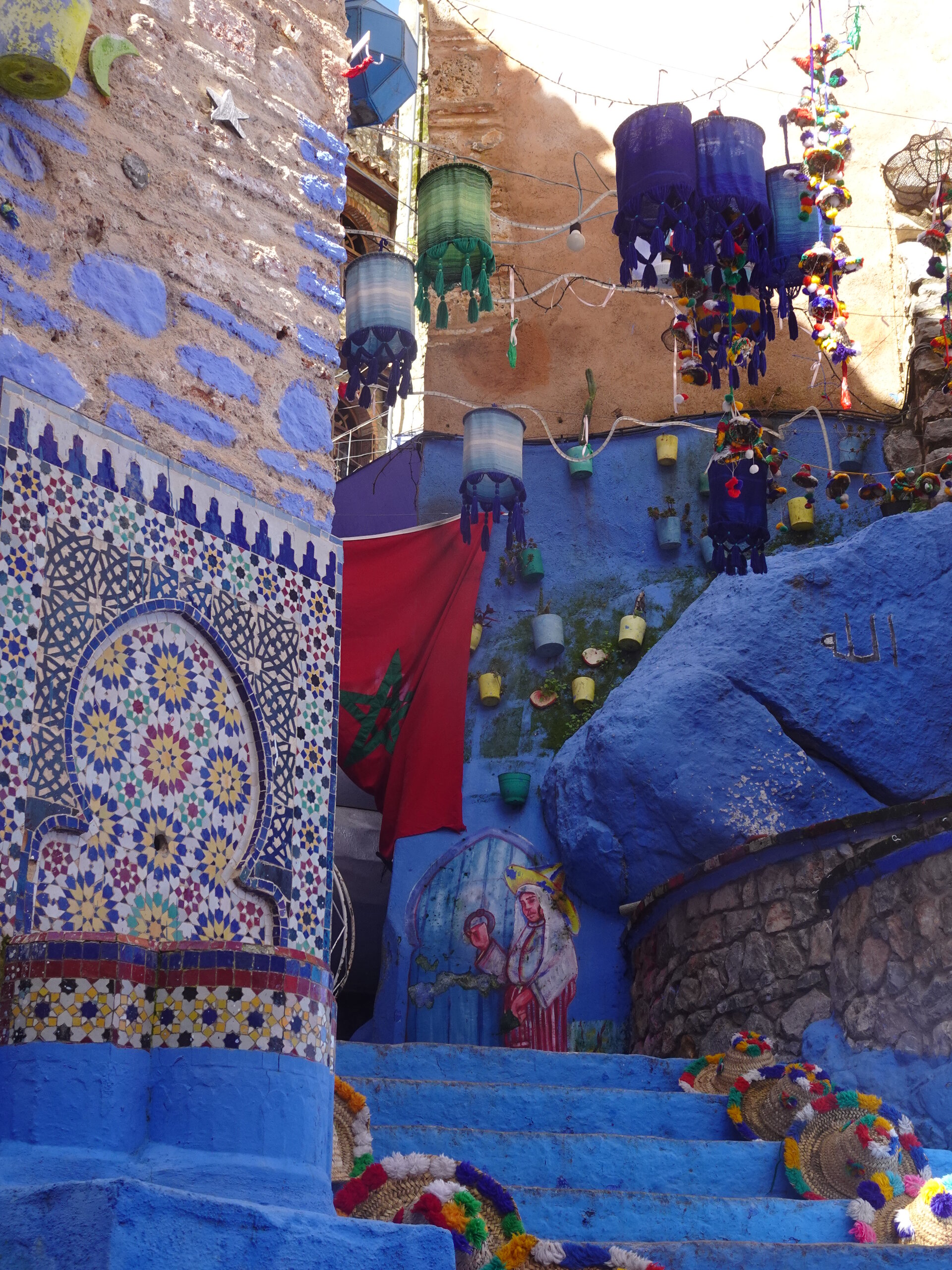 Blue steps with mosaic tilework, hanging lanterns, and Moroccan flag