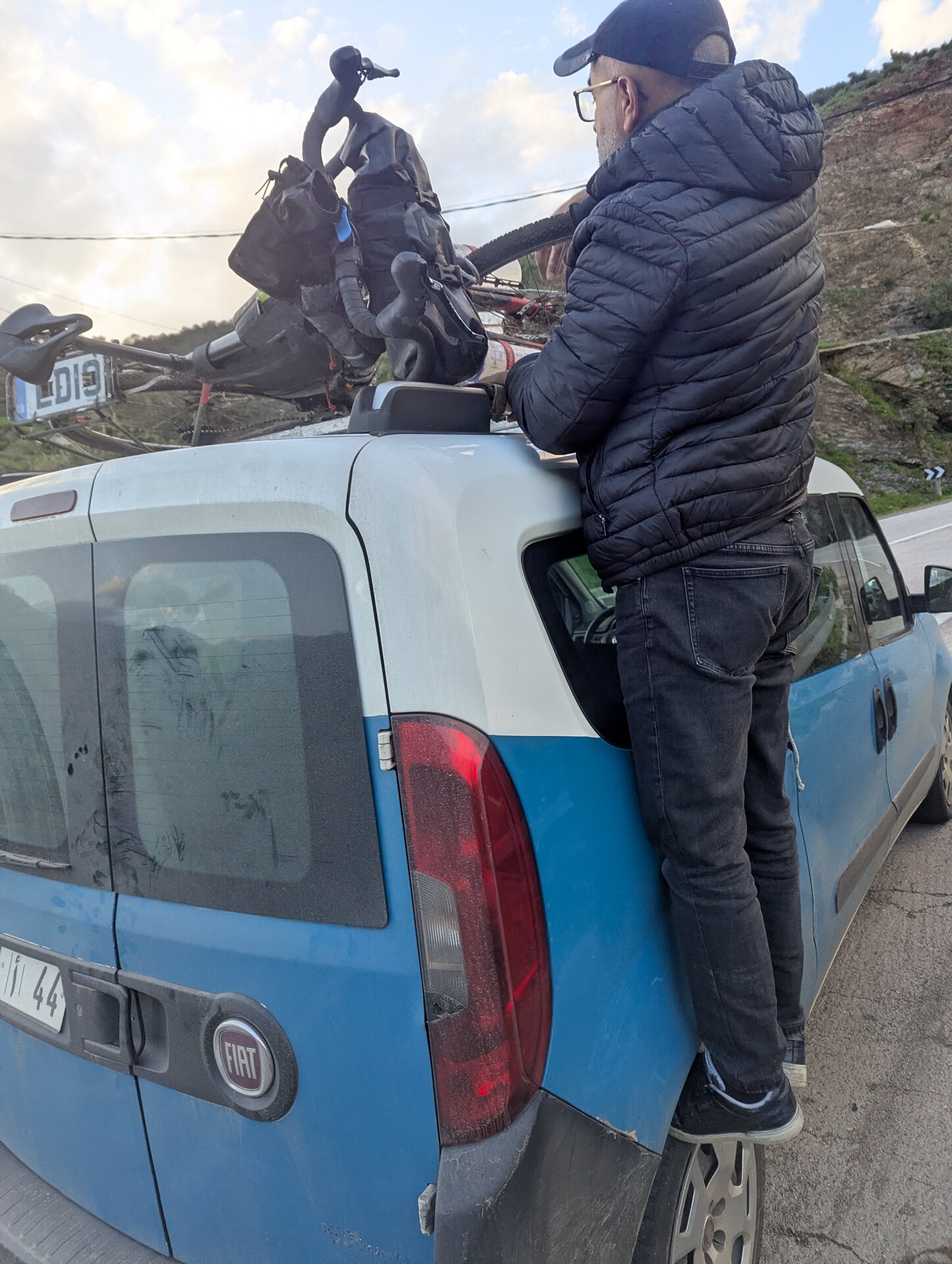 Man loading a bike onto the roof rack of a small blue taxi