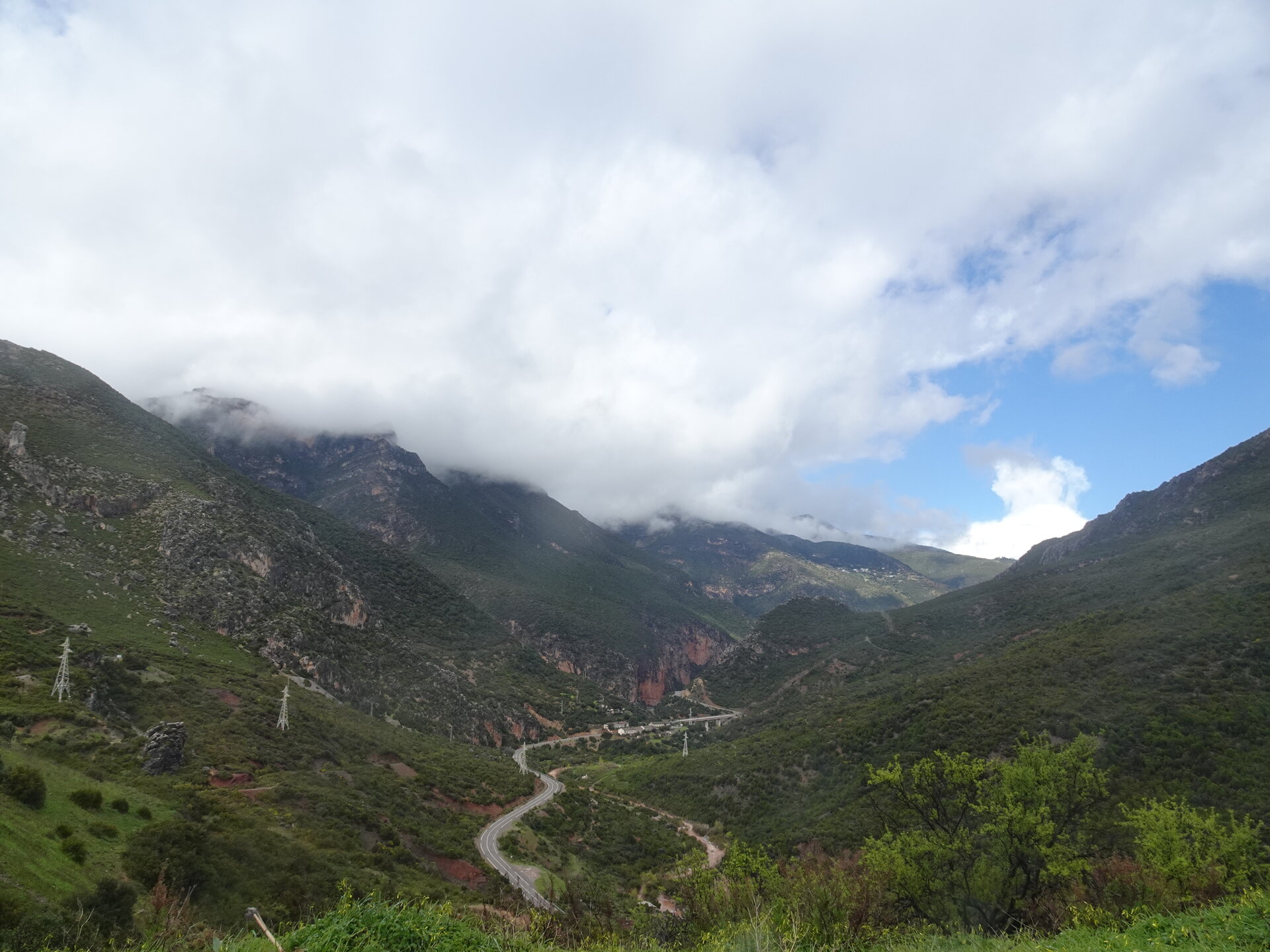 Winding road through a deep green valley with clouds hugging the peaks