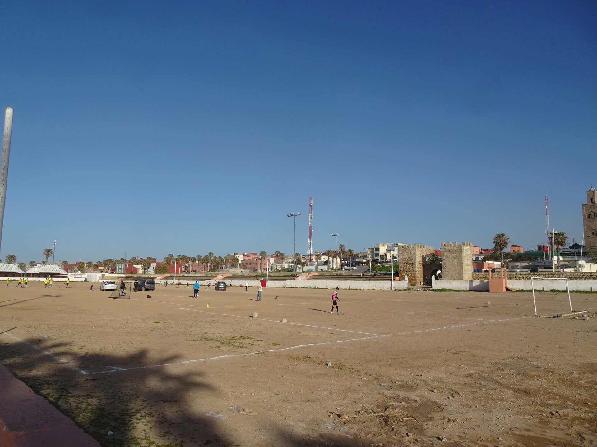 Dusty football pitch with players and old fortress walls in the background
