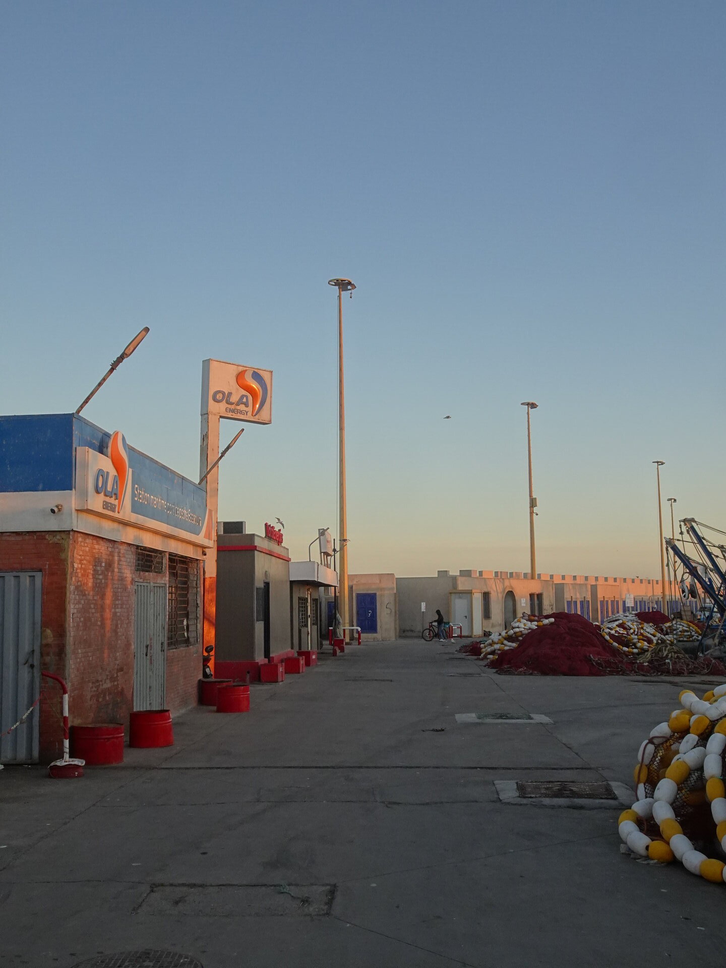 Ola Energy fuel station at the harbour with fishing buoys piled nearby at sunset