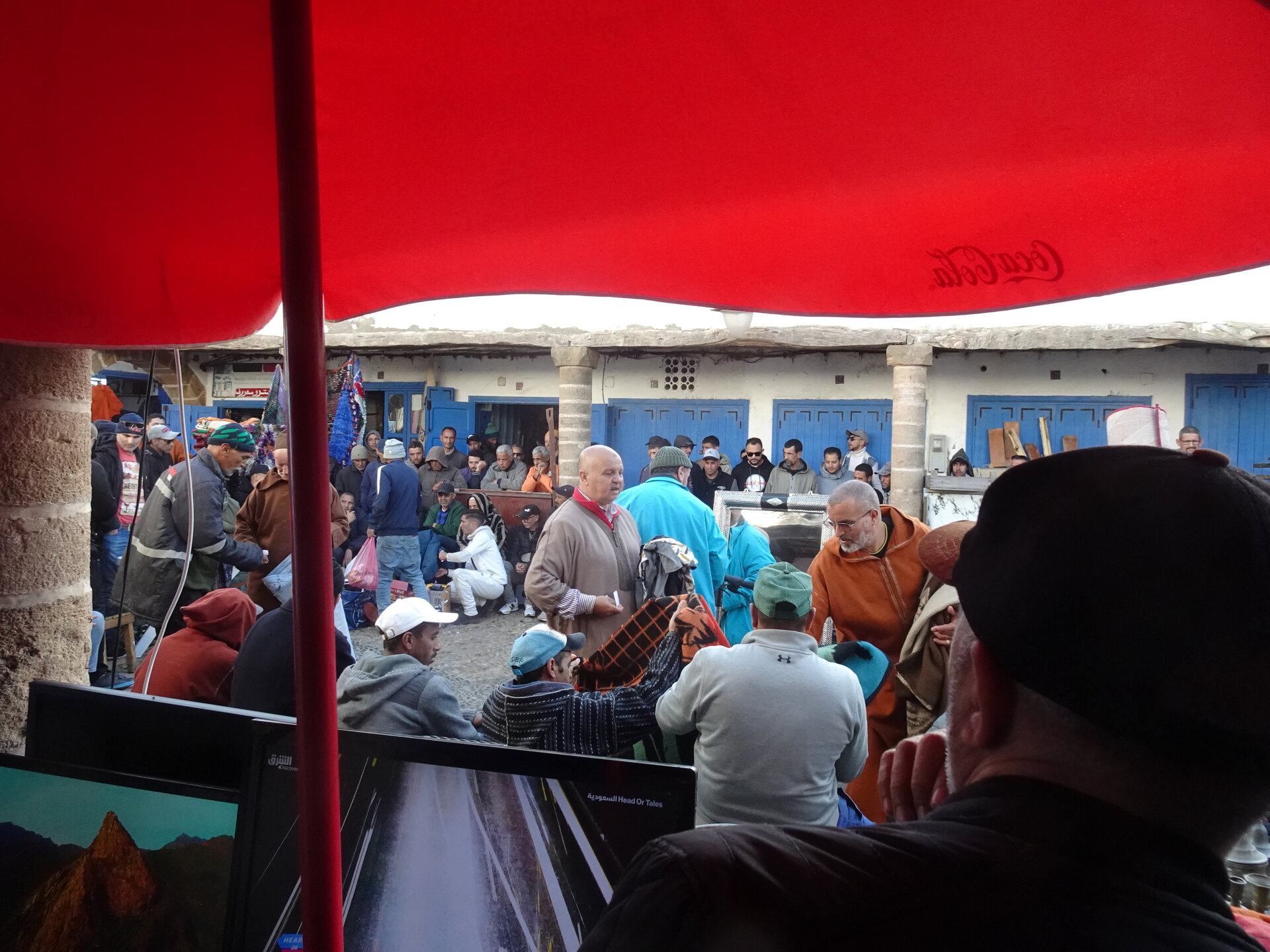 Crowd gathered under a red Coca-Cola parasol watching an outdoor auction