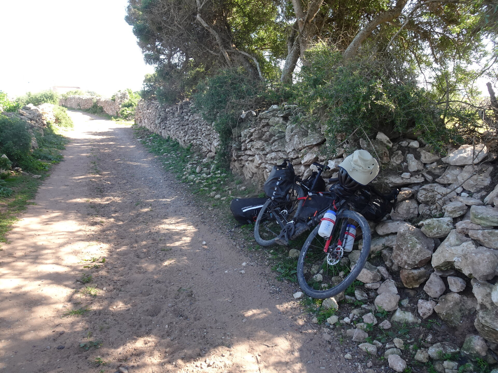 Bikepacking setup leaning against a stone wall on a dirt path shaded by trees