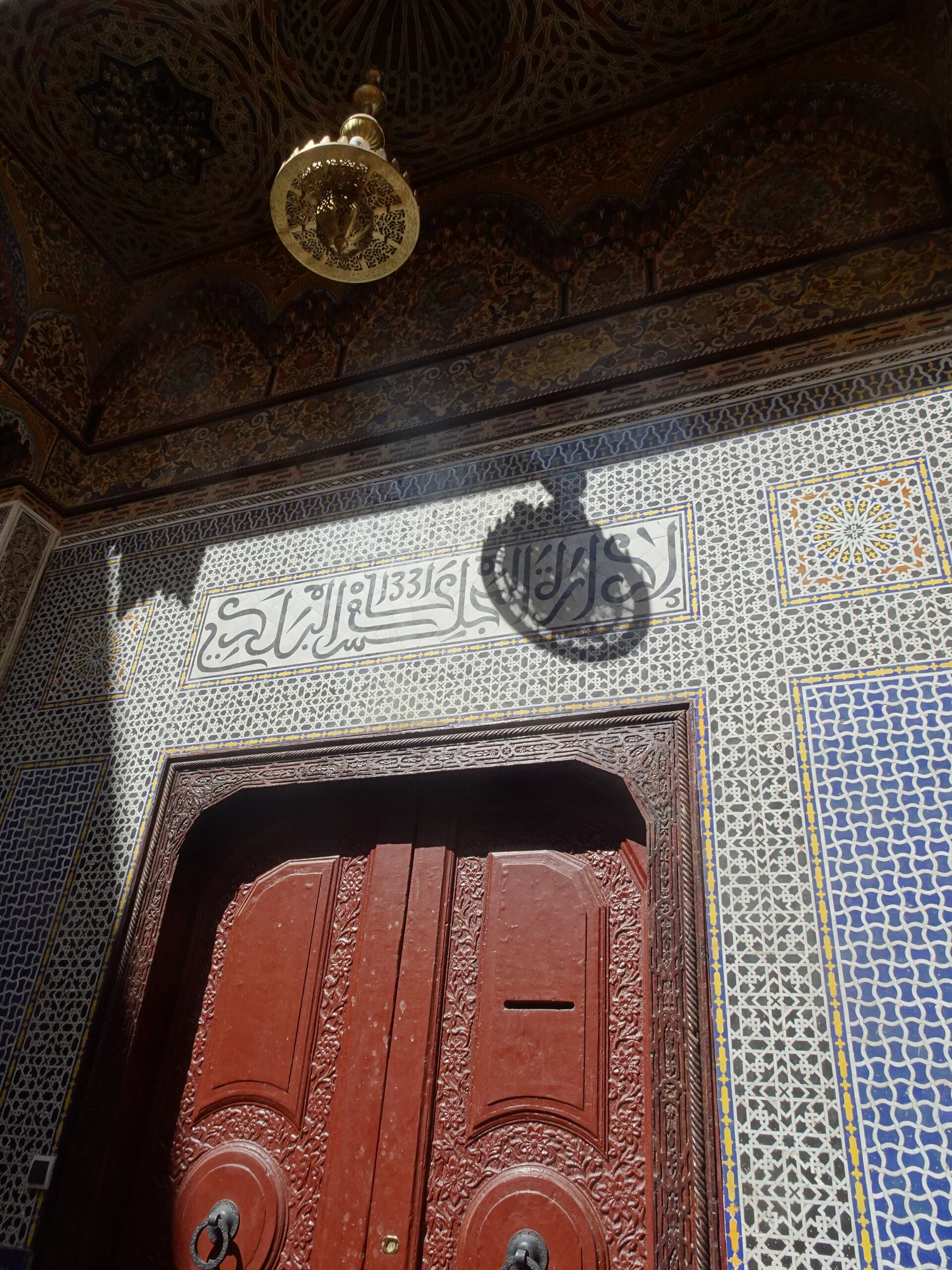 Ornate doorway with carved wood, mosaic tilework, and a brass lantern