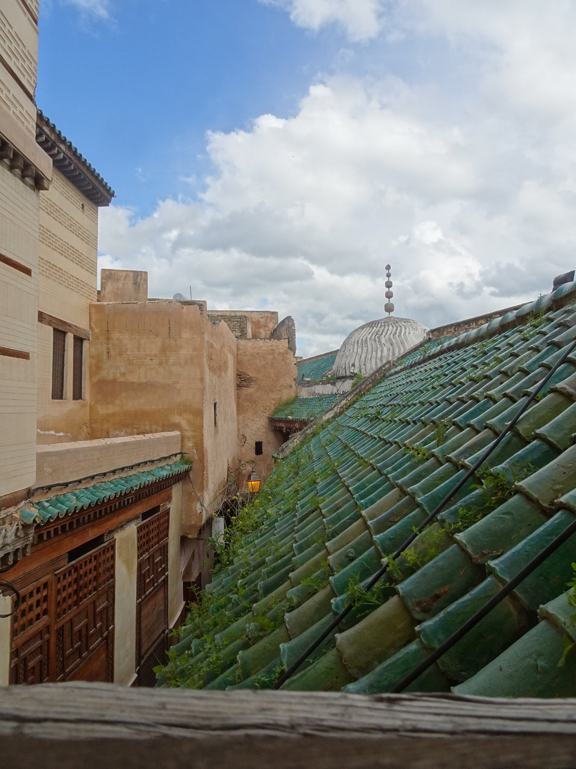 Green tiled rooftop with a mosque dome and minaret rising behind