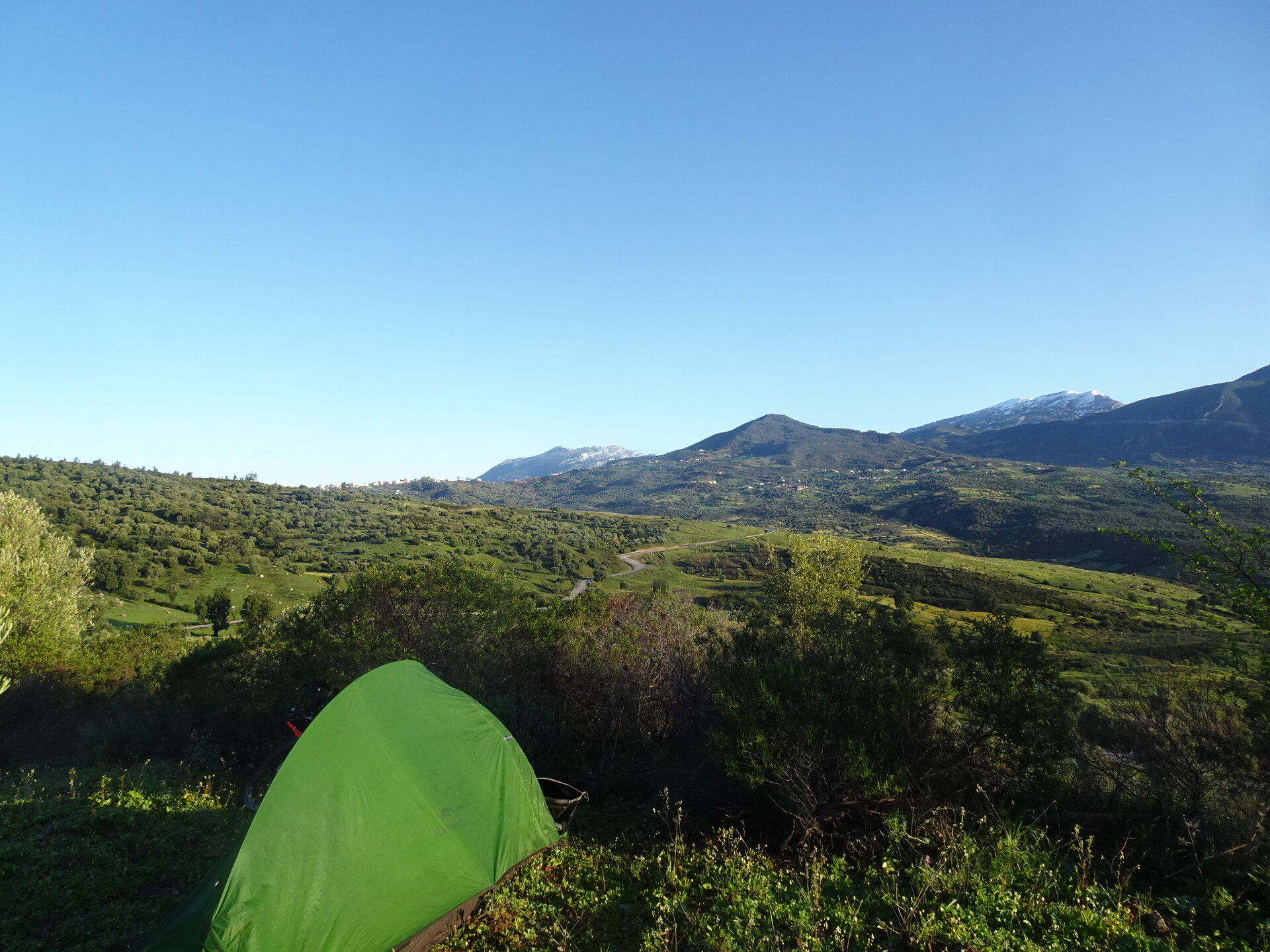 Green tent pitched among bushes with snow-capped Rif mountains behind