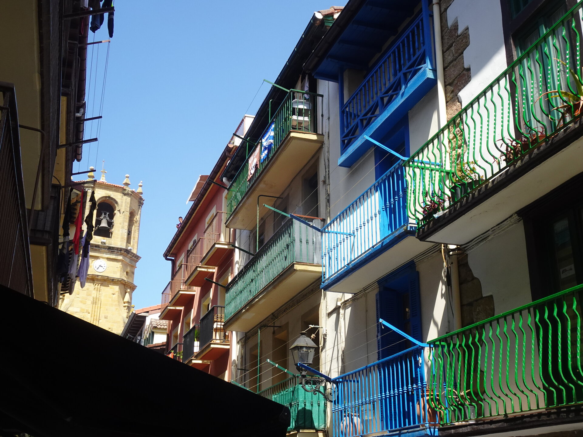 Colourful blue and green balconies with a stone church tower beyond