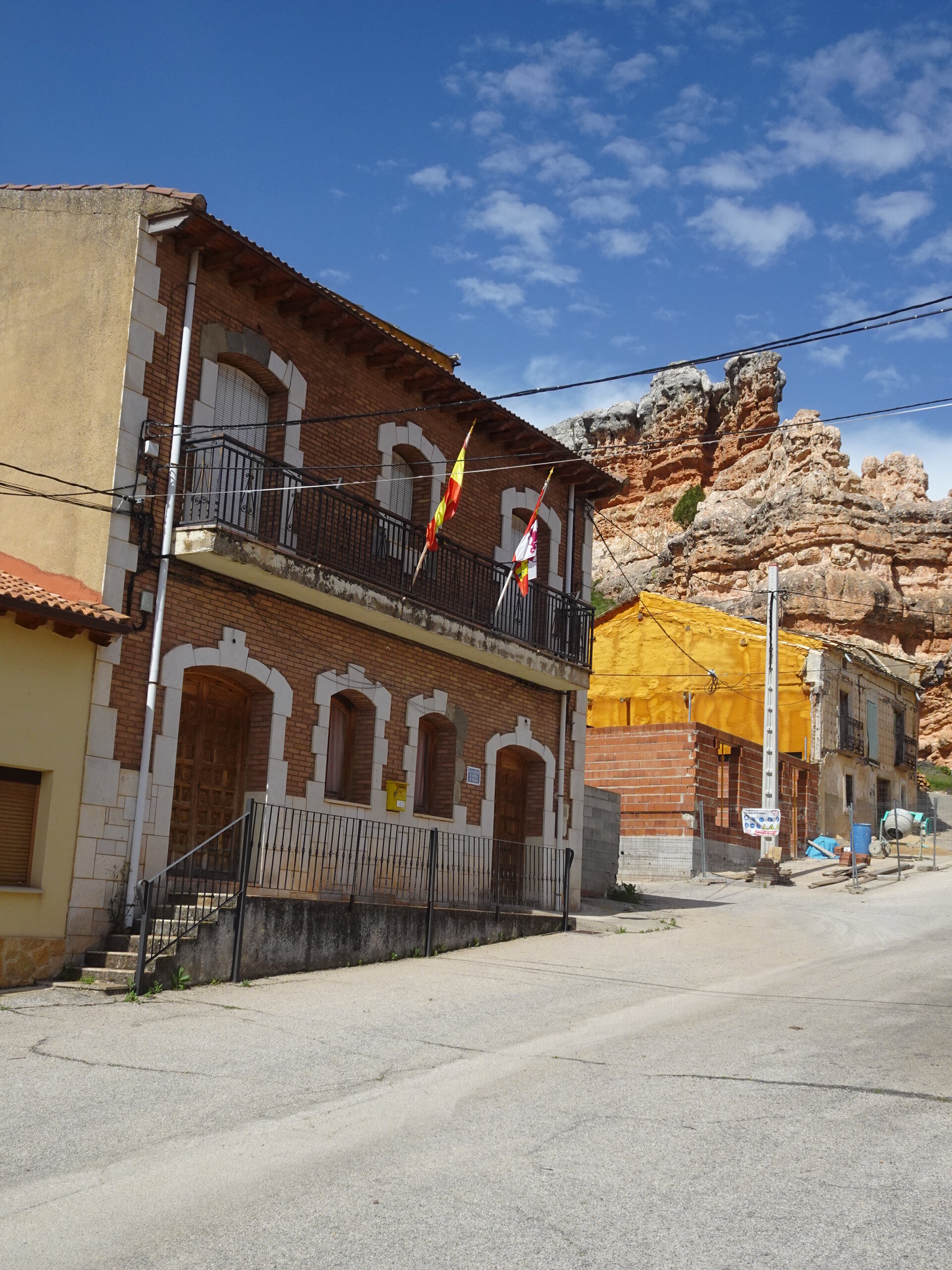 Village street with a brick house flying Spanish flags below red rock cliffs