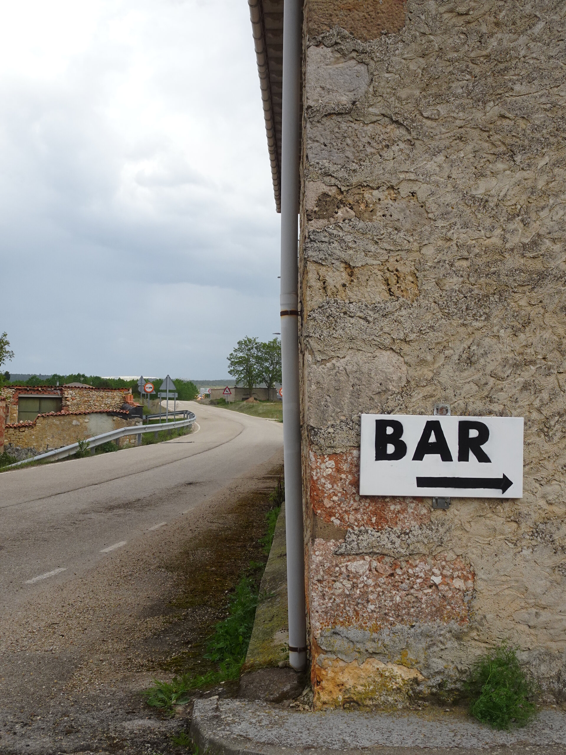 Hand-painted BAR sign on a stone wall beside an empty country road