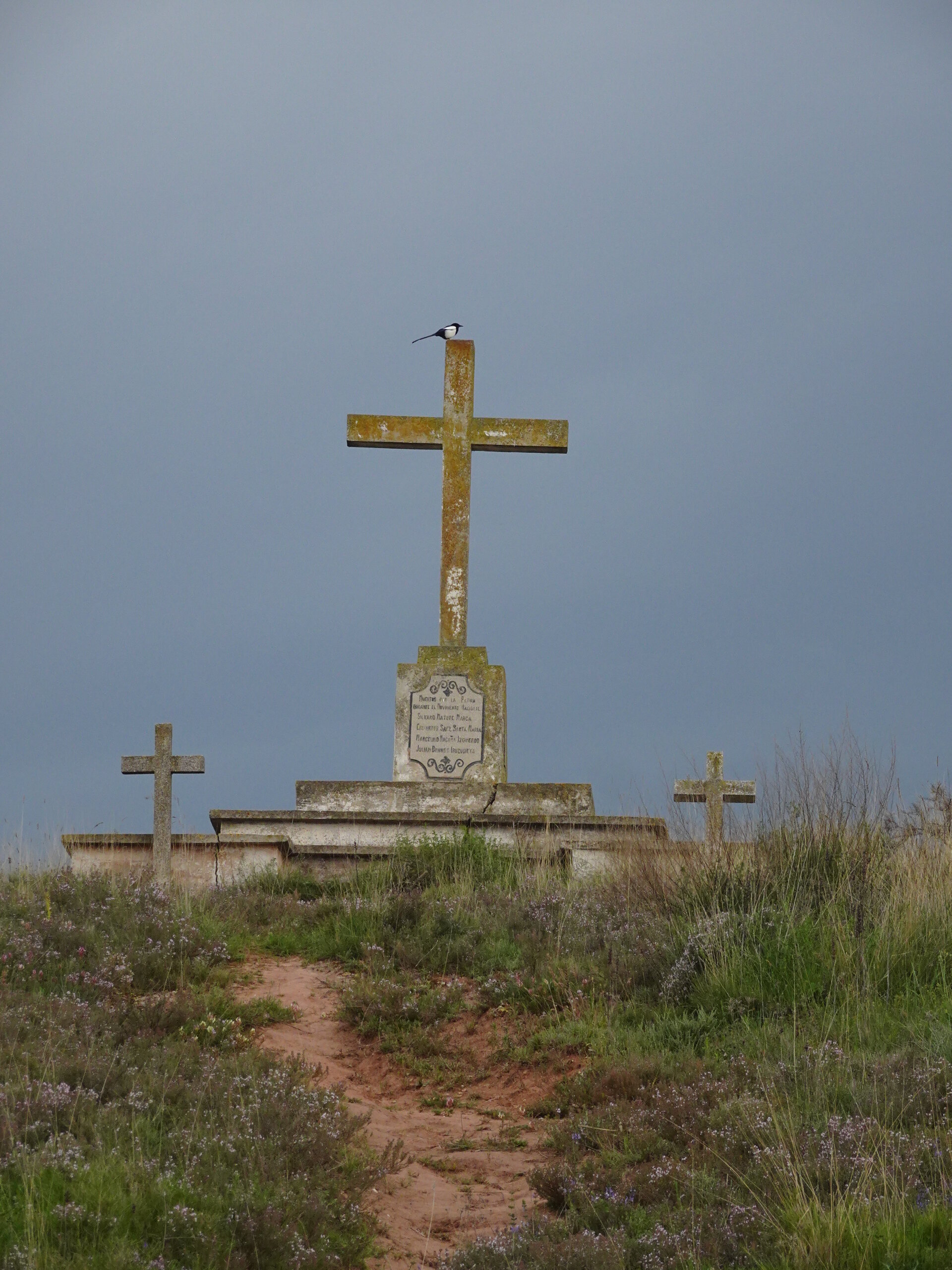 Three weathered stone crosses on a hilltop against a dark stormy sky