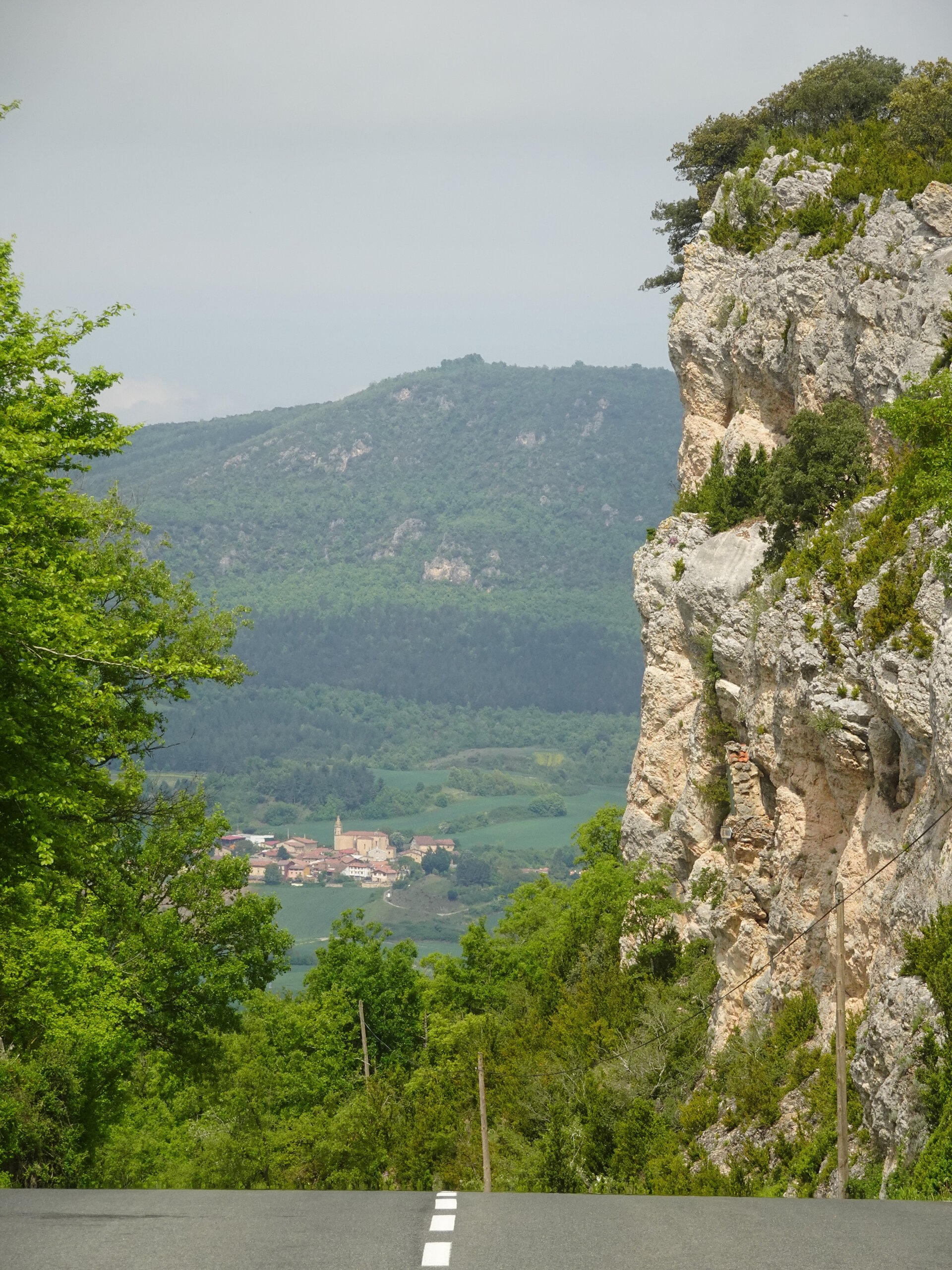 View past a tall rock cliff to a small village in a green valley