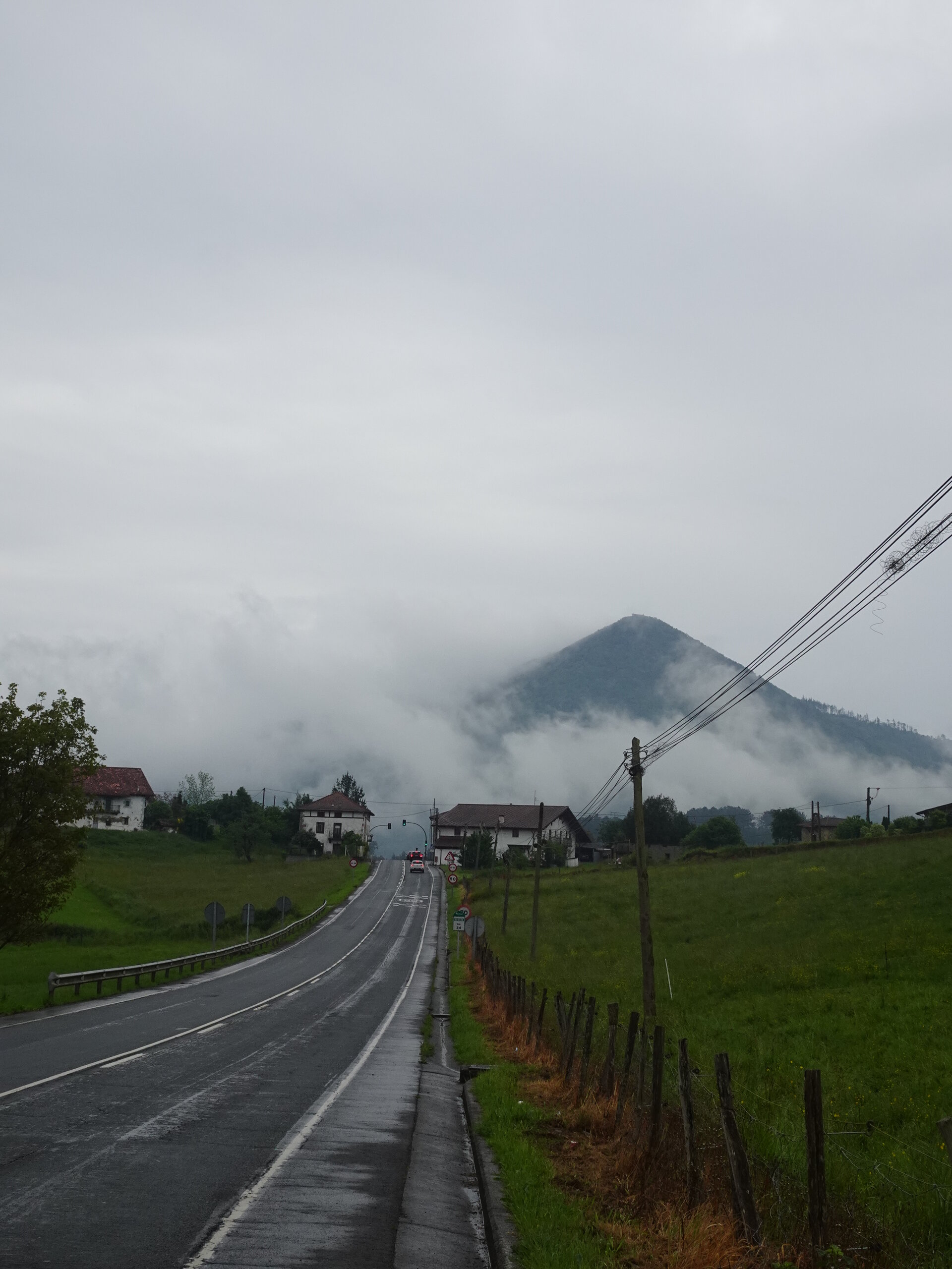 Wet road leading toward a misty conical green mountain past village houses