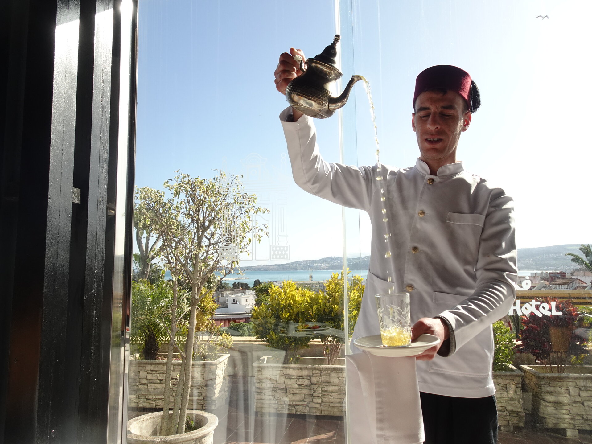 Waiter in fez pouring mint tea from height into a glass