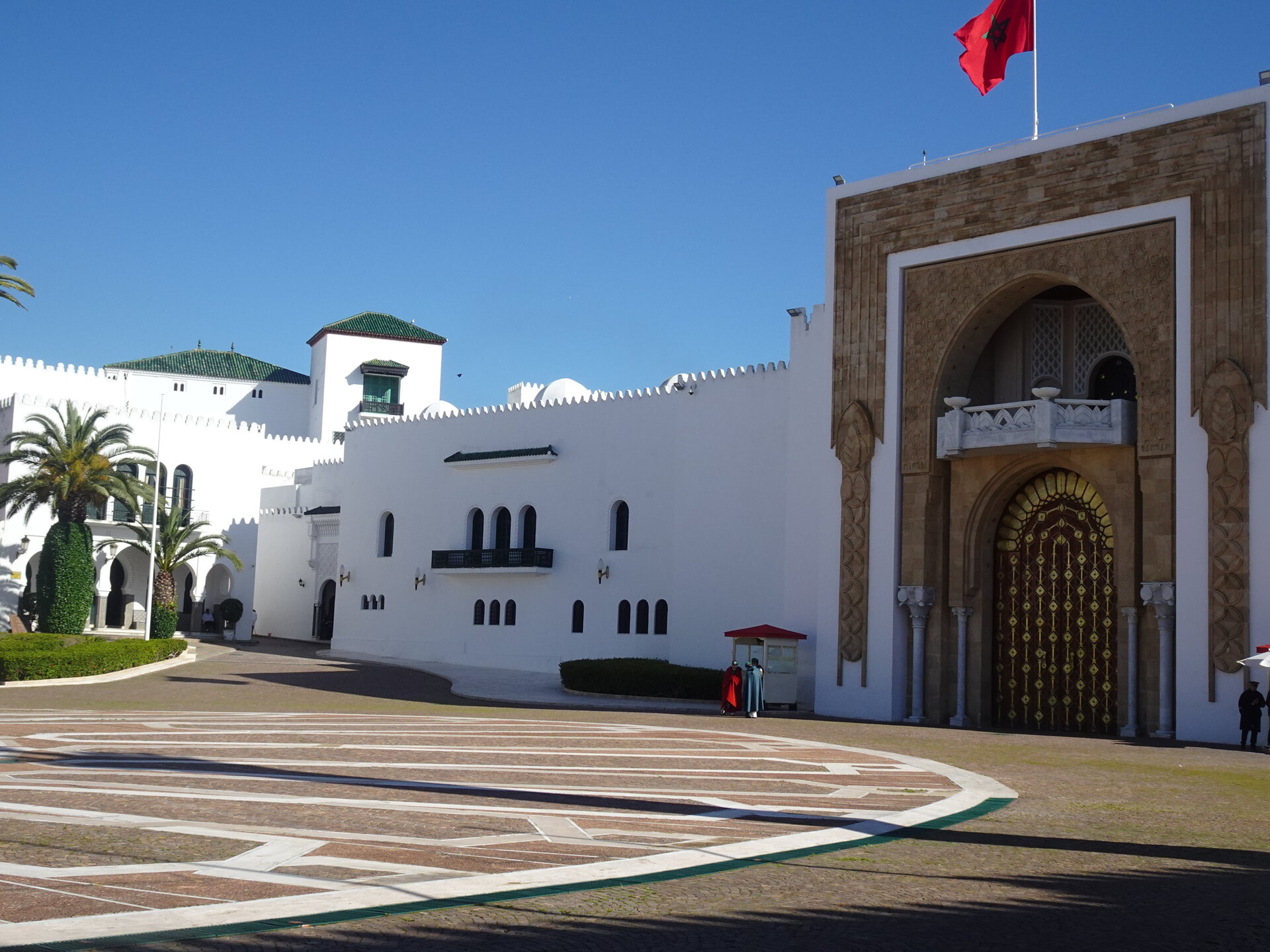 White royal palace with ornate arched entrance and Moroccan flag