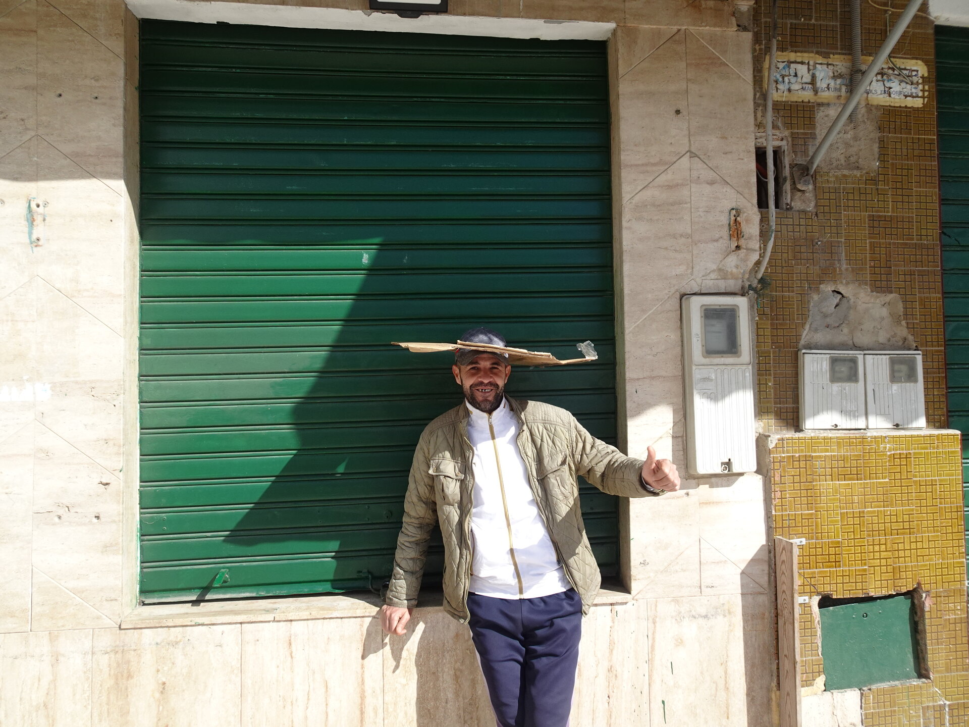Smiling man with a straw hat giving a thumbs up by a green shutter