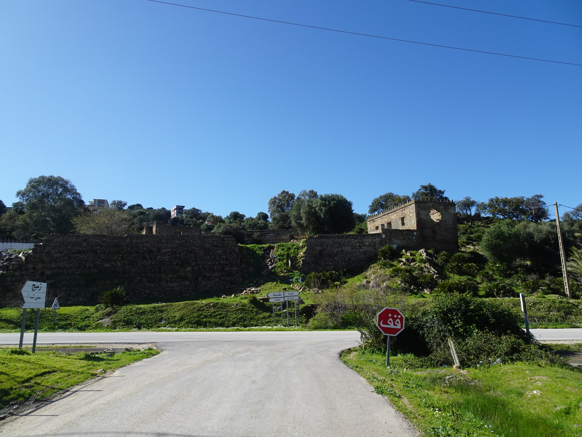 Road junction with Arabic stop sign and old stone ruins on a hill